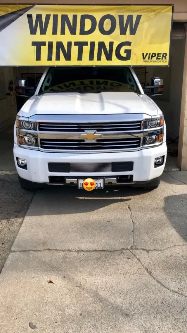White Chevrolet pickup in front of a window tinting banner